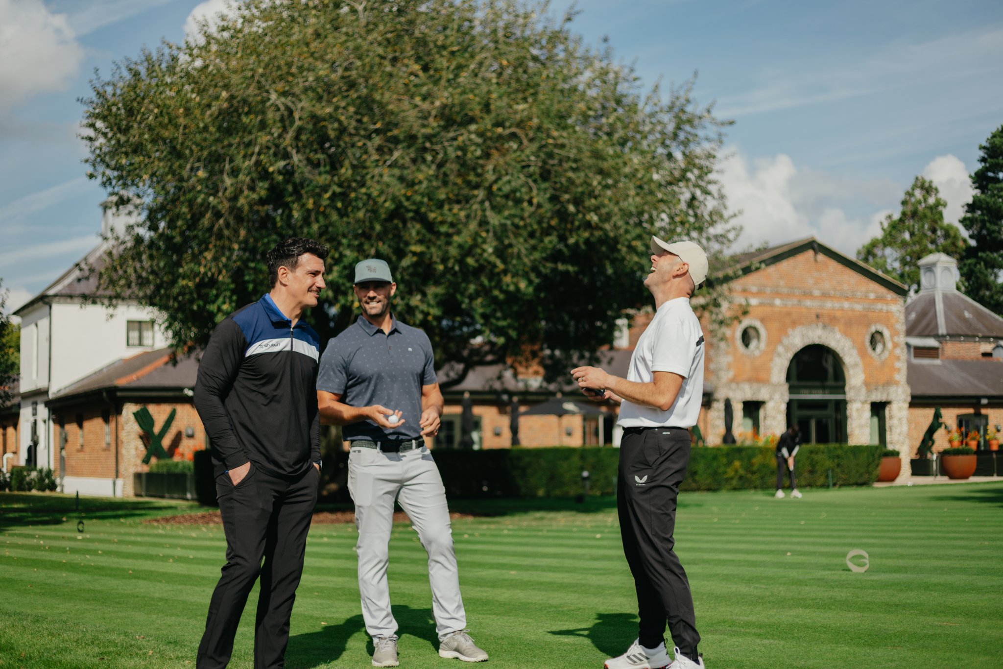 Three men chatting on a golf course during an outdoor event.