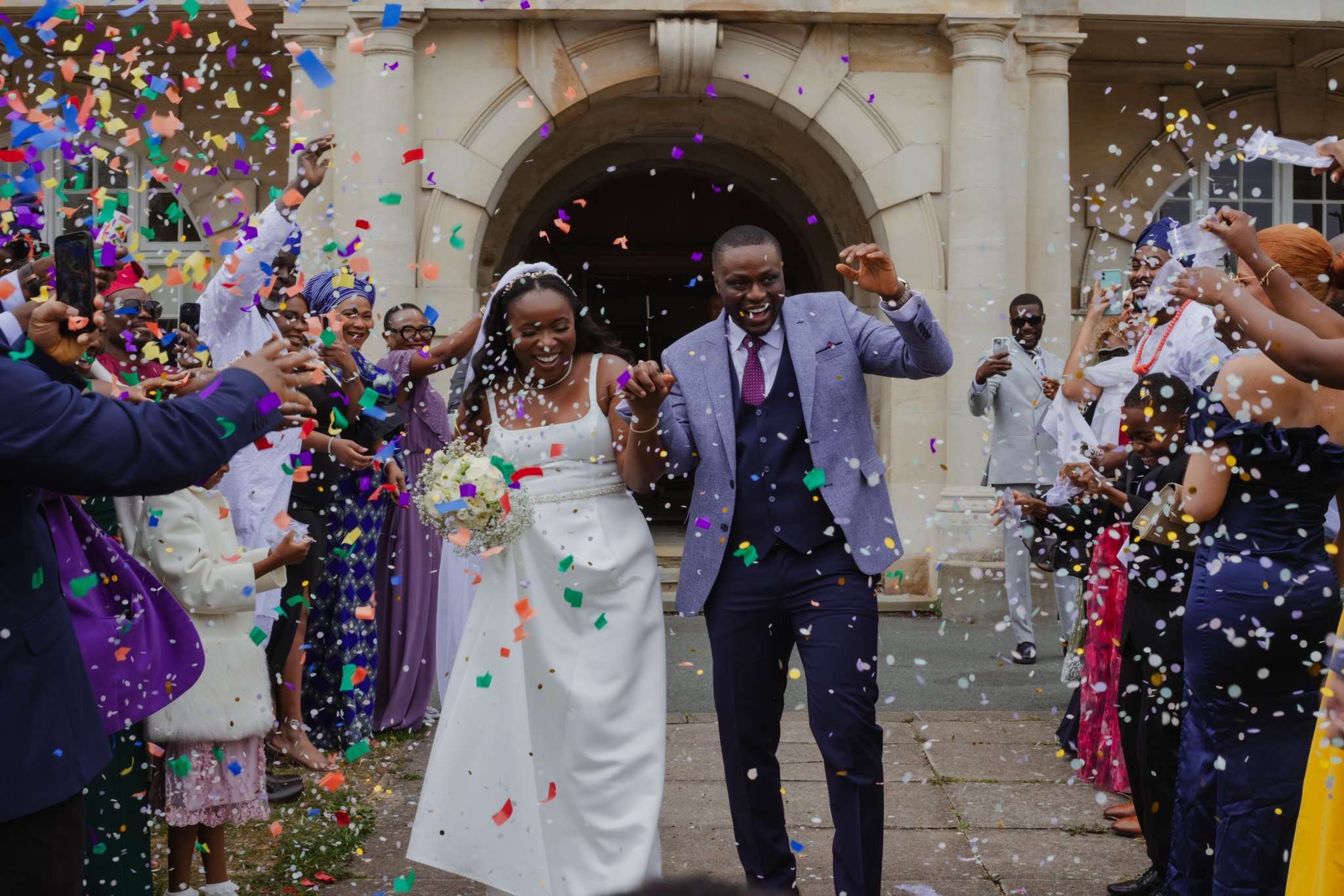 Newly married couple celebrating as colourful confetti falls around them outside the ceremony venue.