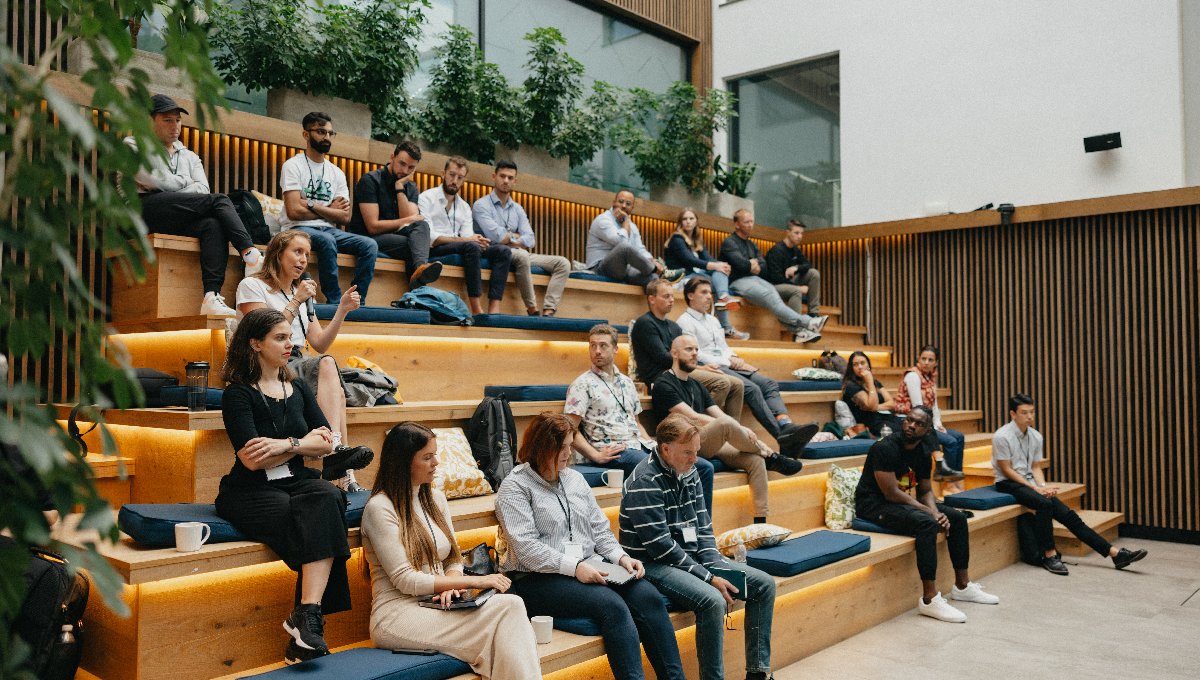 Attendees seated on tiered wooden benches during a business event.