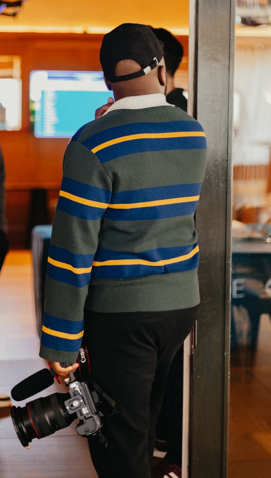 Lionel Odelana seen from behind wearing a striped jumper at an indoor event. Lionel Odelana