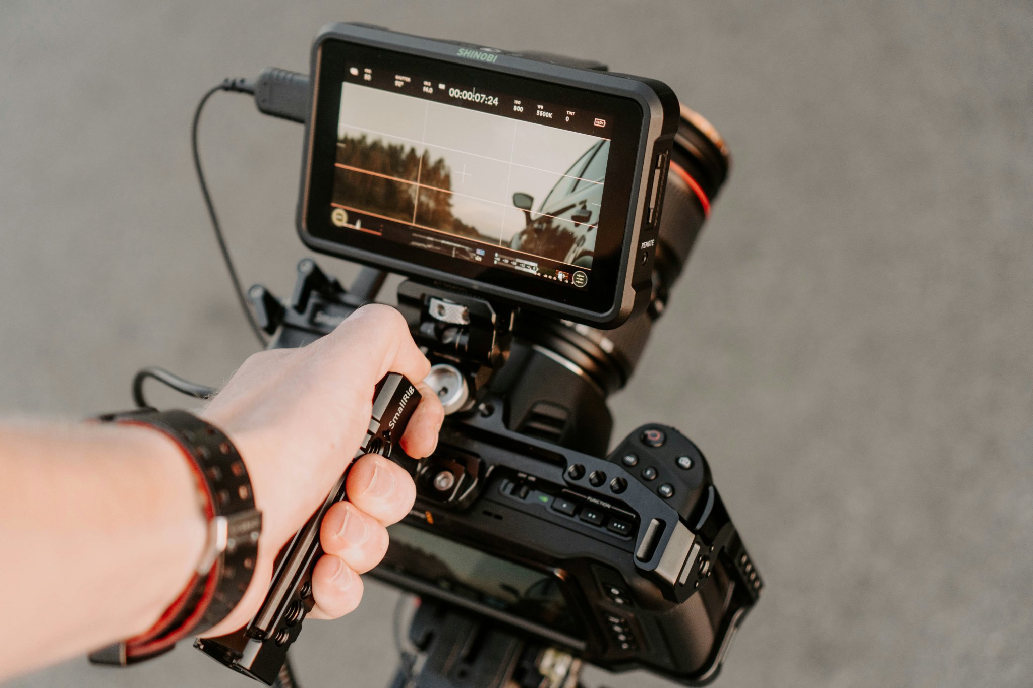 Hand holding a professional camera rig with an external monitor showing an outdoor scene.