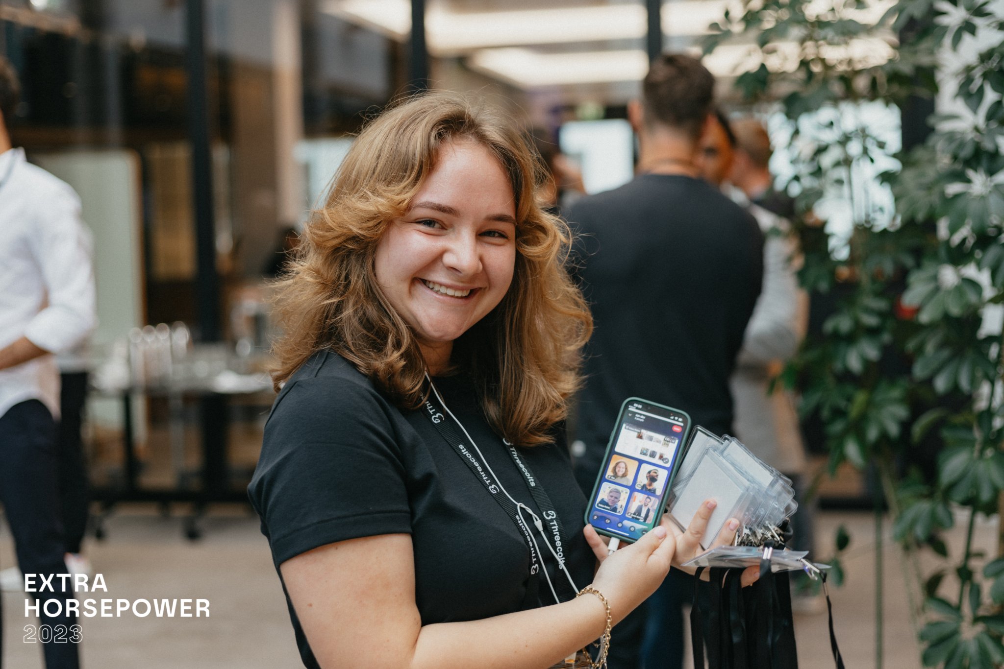 Smiling woman holding up a smartphone during a business event.