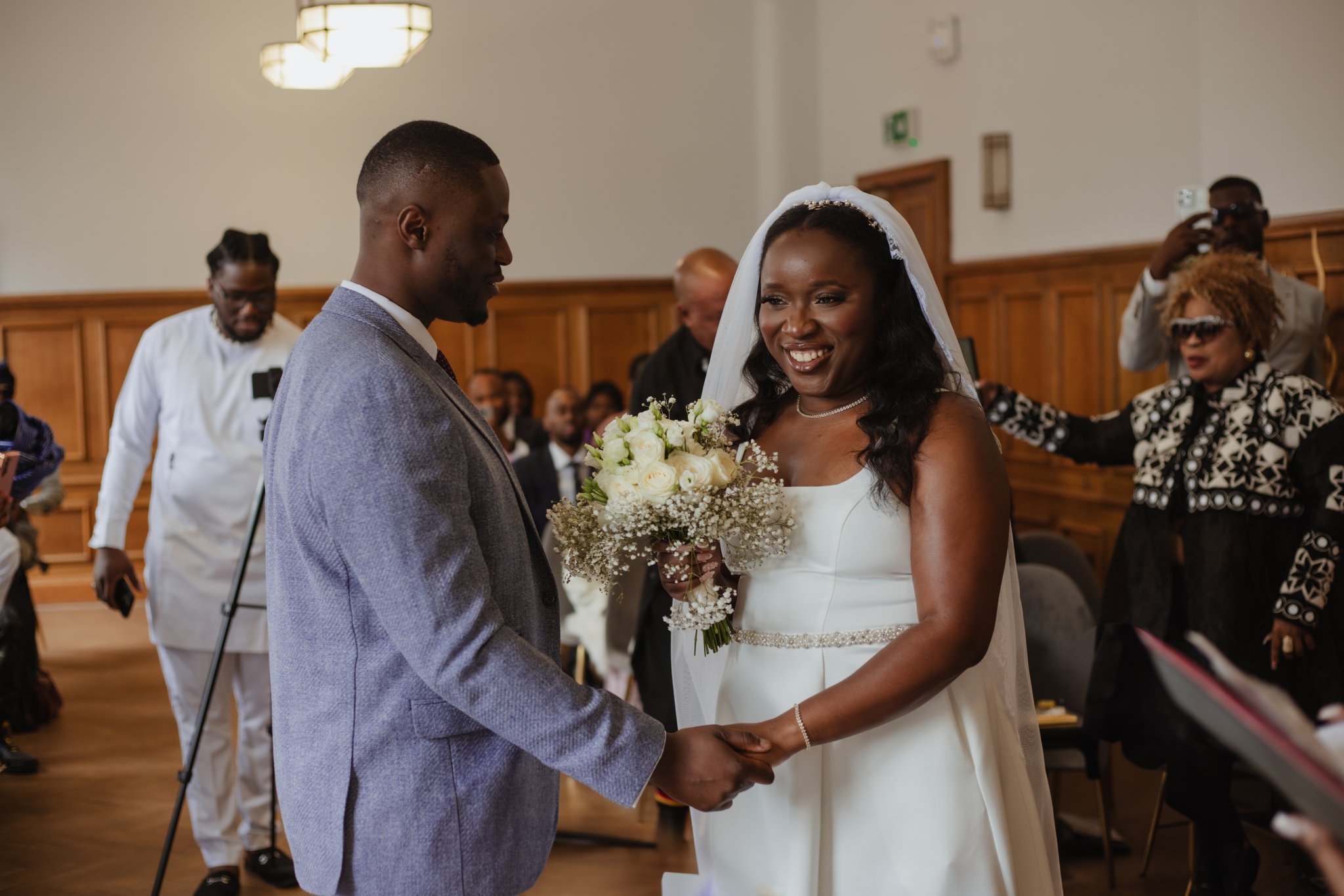 Bride and groom holding hands and smiling at each other during their indoor wedding ceremony.