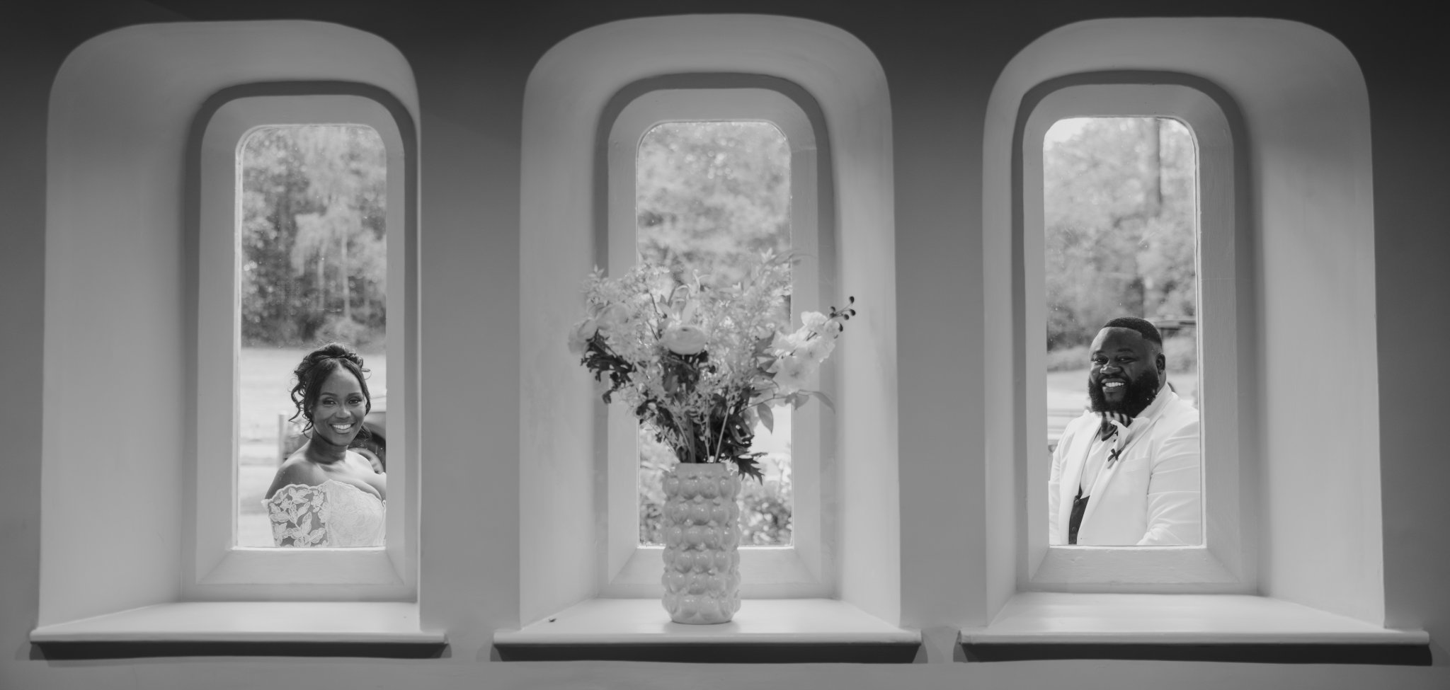 Black-and-white photograph of a flower arrangement in a vase on a windowsill.