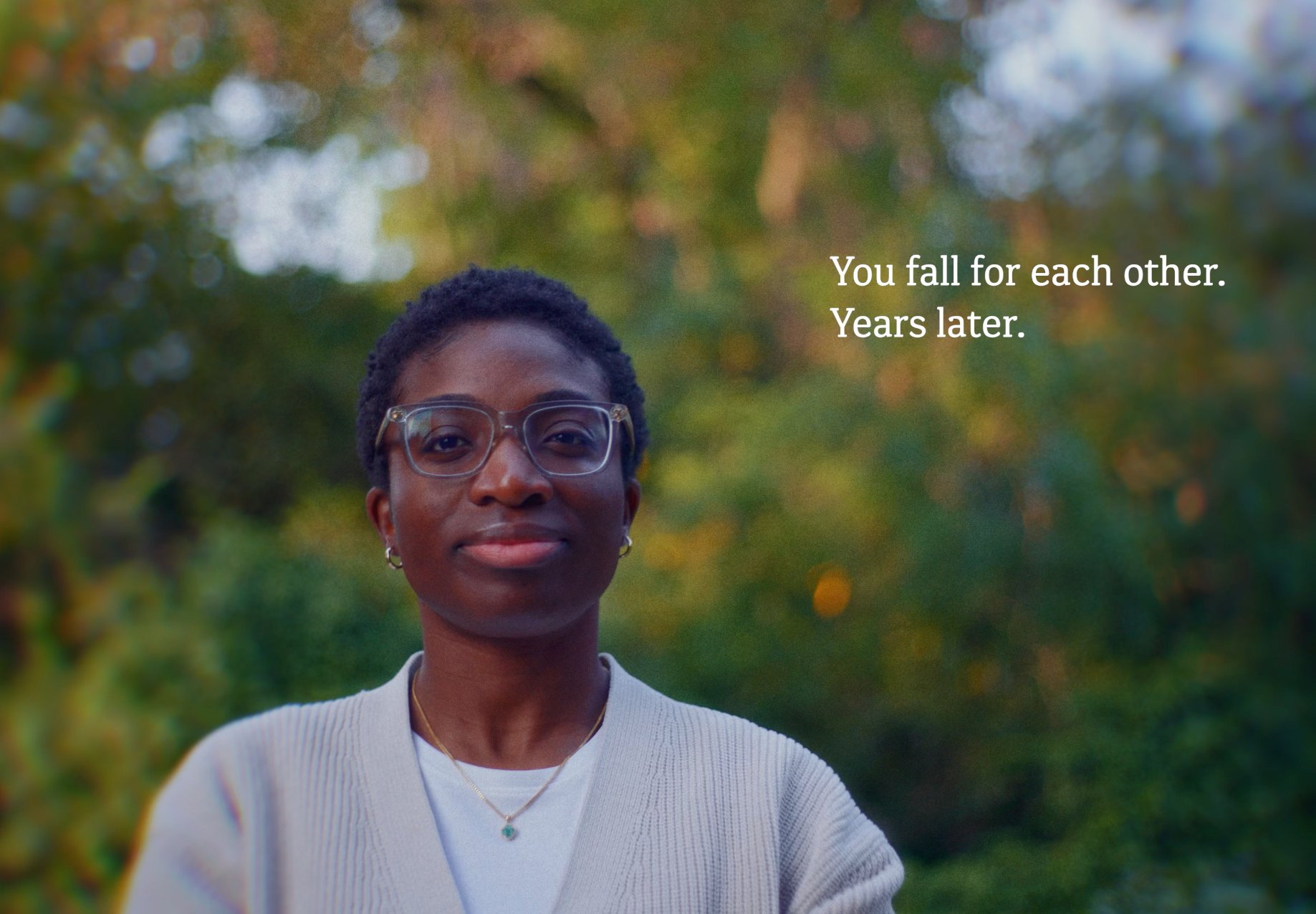 Cinematic outdoor portrait of a black woman with short natural hair and glasses, looking directly at the camera against a softly blurred green background.