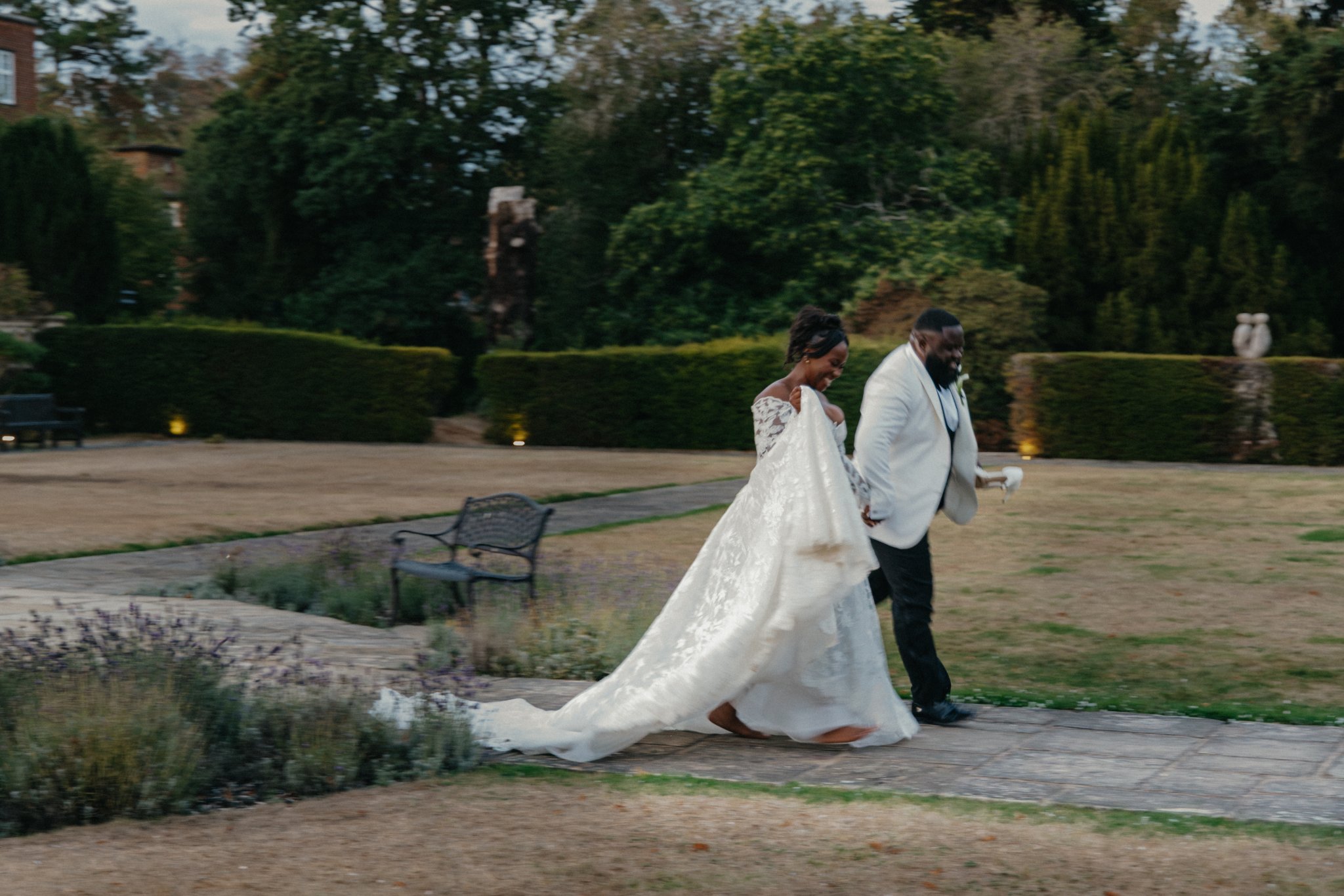 Bride and groom walking together through a garden, with the bride's long wedding dress trailing behind her.