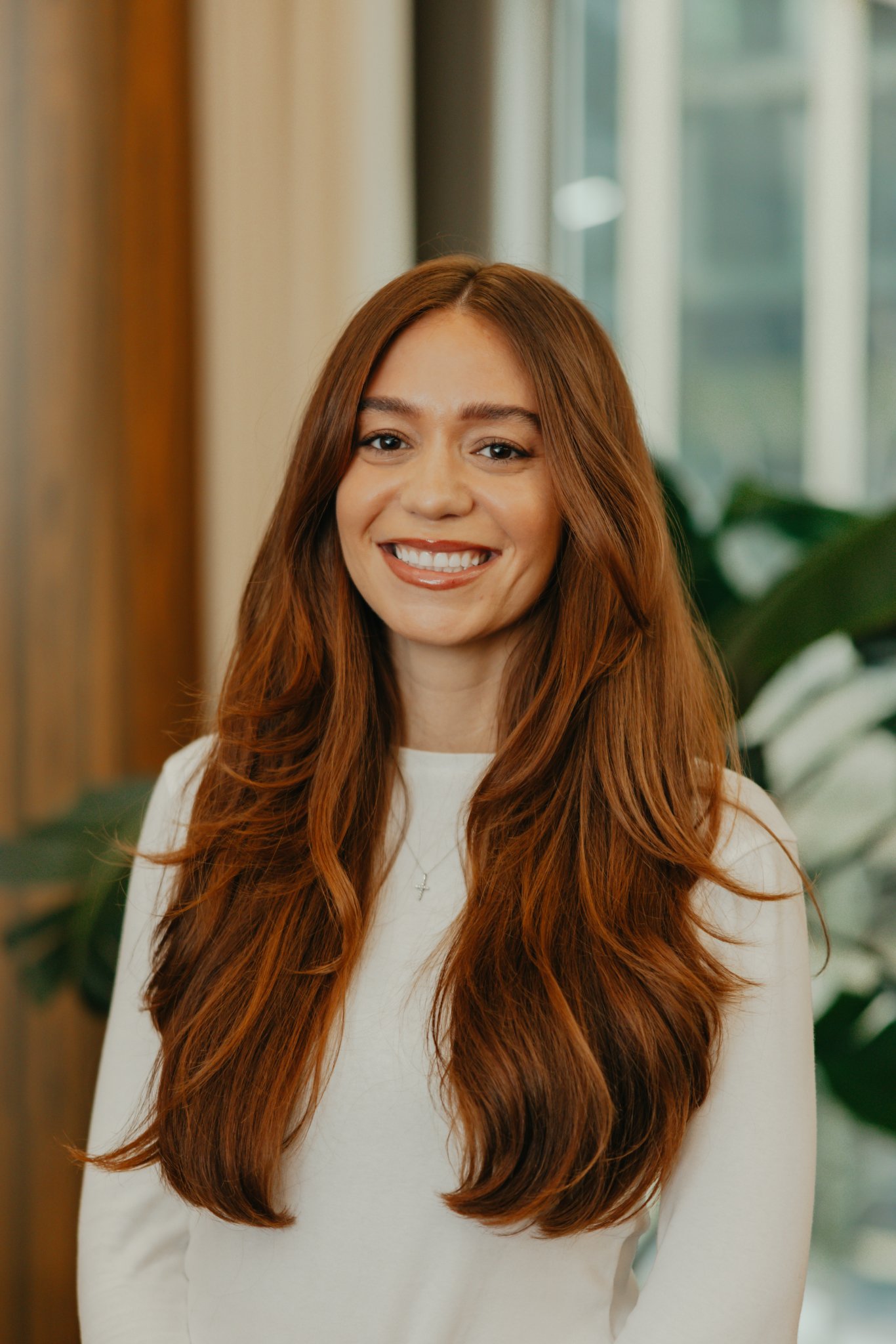 Professional headshot of a smiling woman with long auburn hair wearing a white top.