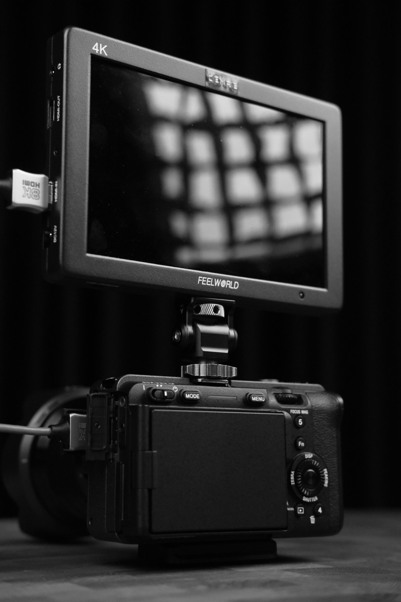 Black-and-white photograph of a camera rig with a Feelworld monitor displaying a grid of bright lights.