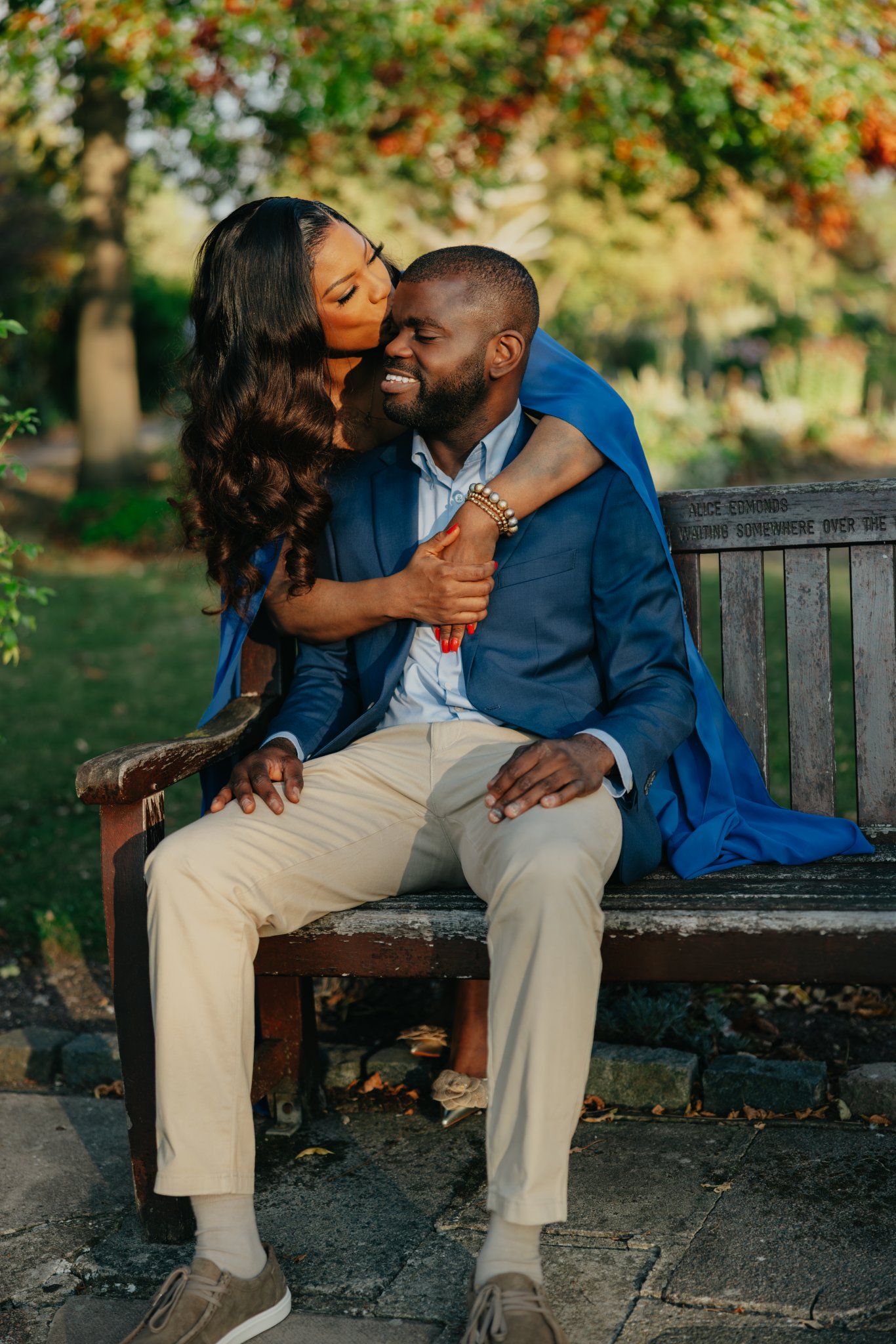 Couple embracing on a wooden bench surrounded by warm, sunlit greenery.