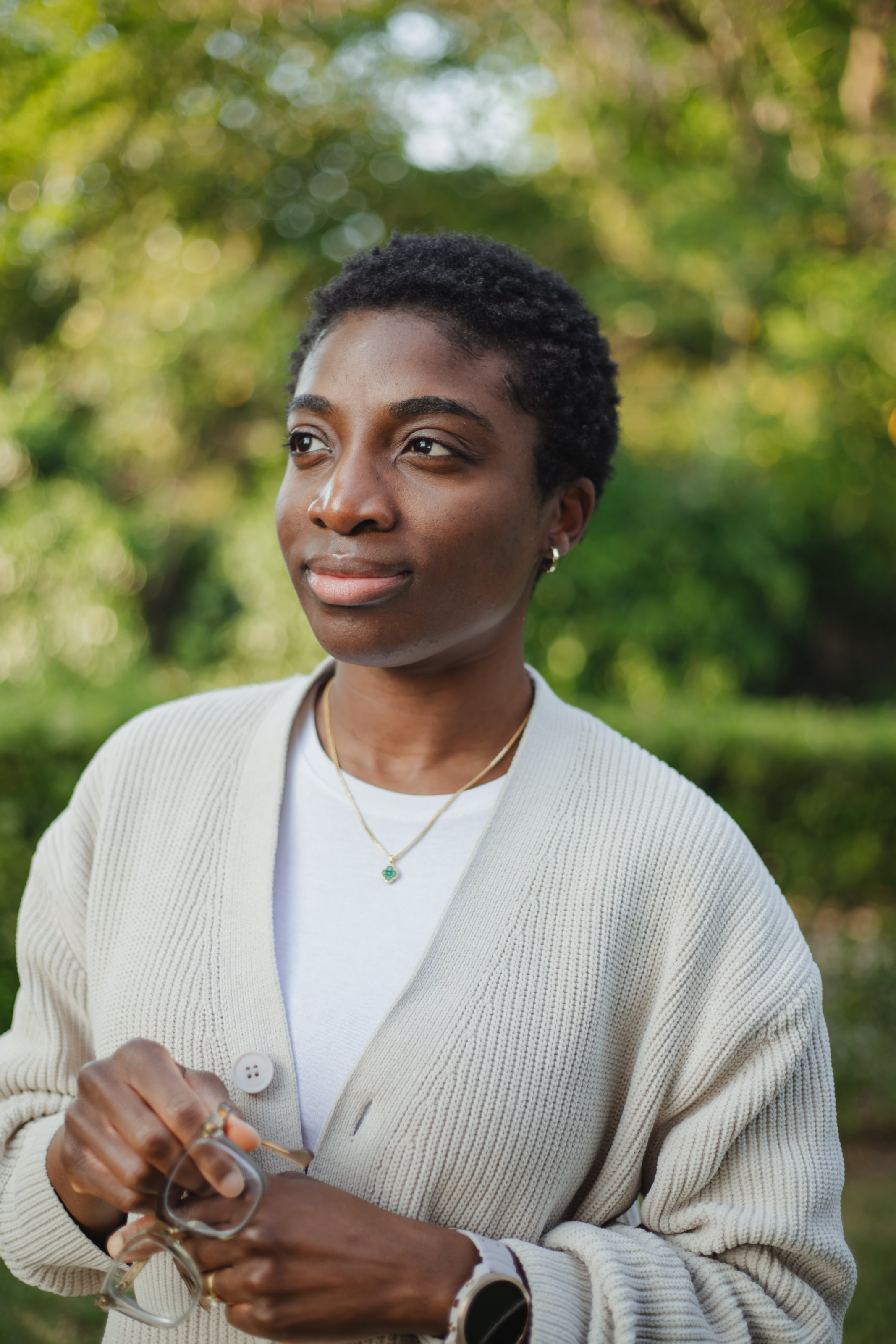 Outdoor portrait of Judy Odelana wearing a light-coloured cardigan against a softly blurred green background.