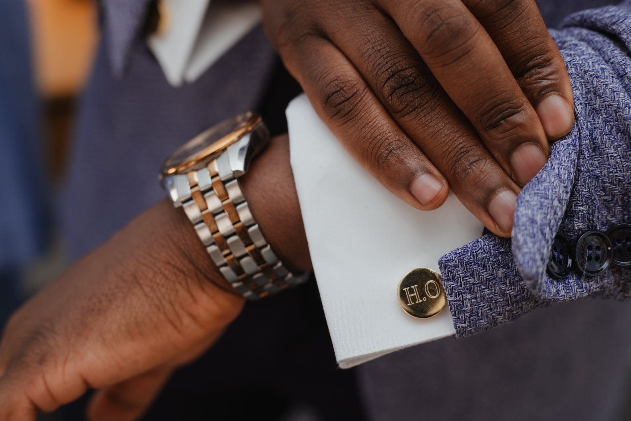 Close-up of a groom's wristwatch, hand and personalised cufflink against a white shirt cuff.